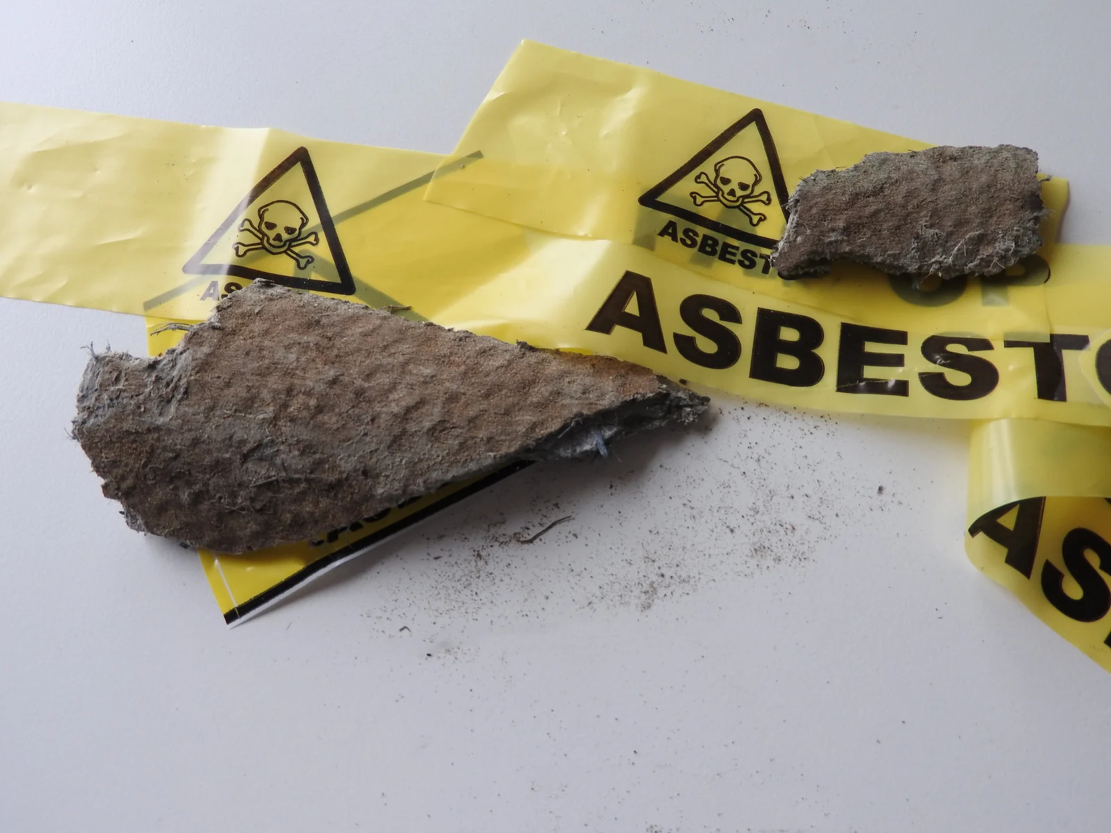 Brokstuk asbesthoudend materiaal op geel afzetlint met asbestwaarschuwing
