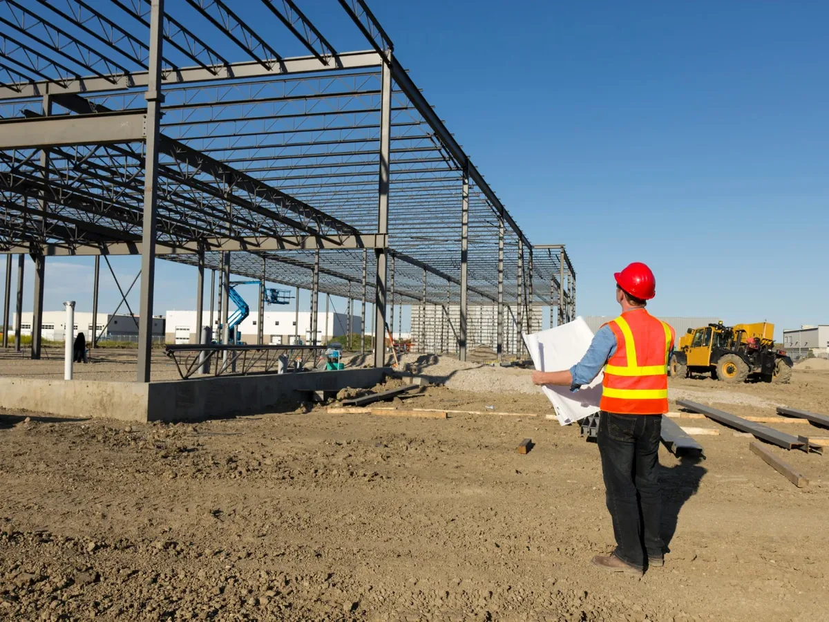 Veiligheidscoördinator met bouwplannen op een werf met staalconstructie in opbouw